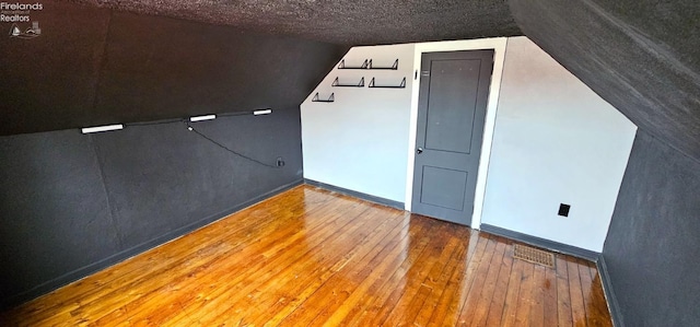 bonus room with baseboards, vaulted ceiling, hardwood / wood-style flooring, and a textured ceiling