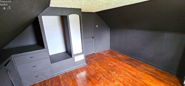 additional living space with a textured ceiling, wood finished floors, baseboards, and lofted ceiling