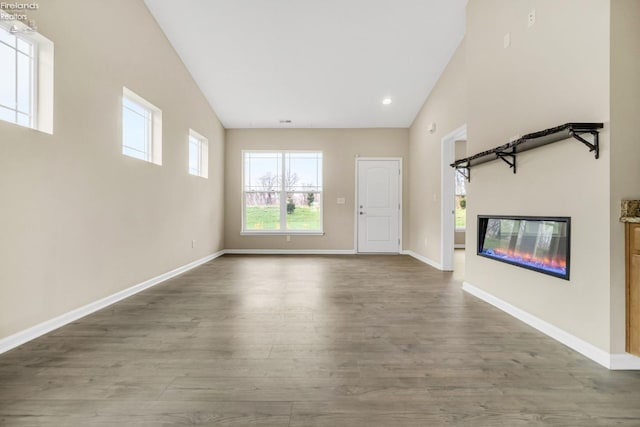 unfurnished living room featuring recessed lighting, a glass covered fireplace, wood finished floors, and baseboards