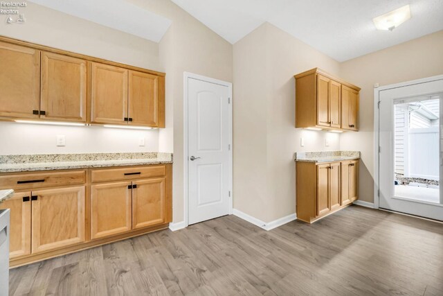 kitchen featuring light wood-style flooring, light stone countertops, light brown cabinets, and baseboards