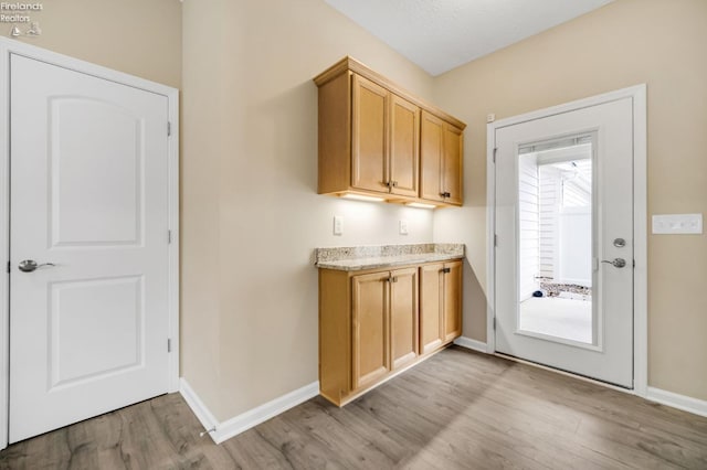 kitchen featuring light stone countertops, light wood finished floors, and baseboards