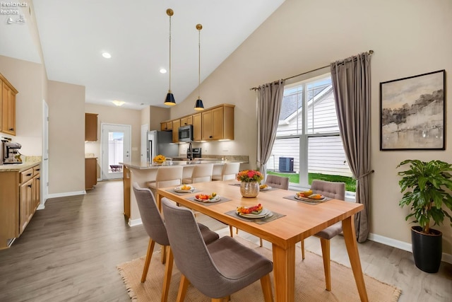 dining space with a wealth of natural light, baseboards, high vaulted ceiling, and light wood-style floors