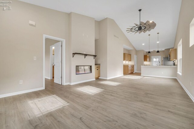 unfurnished living room with visible vents, a sink, light wood-style floors, baseboards, and high vaulted ceiling