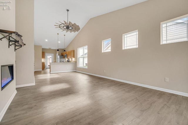 unfurnished living room featuring high vaulted ceiling, baseboards, a ceiling fan, and wood finished floors
