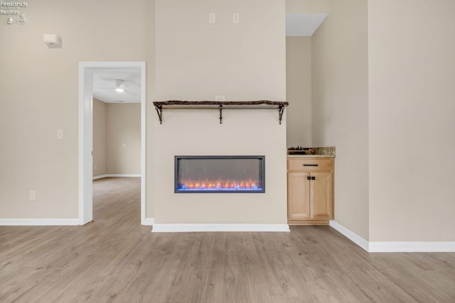 unfurnished living room featuring baseboards, a glass covered fireplace, and light wood finished floors