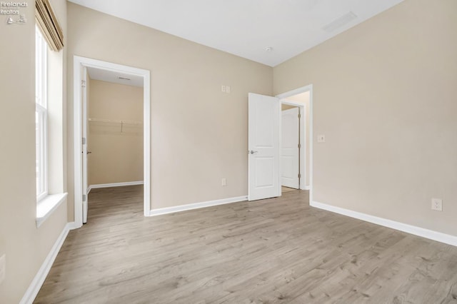 unfurnished bedroom with a walk in closet, baseboards, and light wood-type flooring