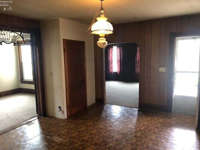 unfurnished dining area featuring wooden walls, carpet floors, and arched walkways