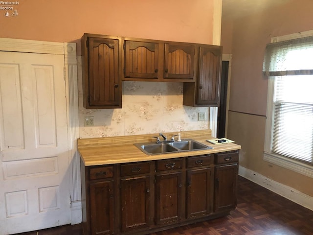 kitchen with baseboards, a sink, light countertops, dark brown cabinetry, and wallpapered walls