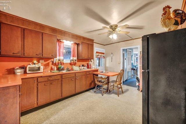kitchen with light countertops, brown cabinets, freestanding refrigerator, and ceiling fan
