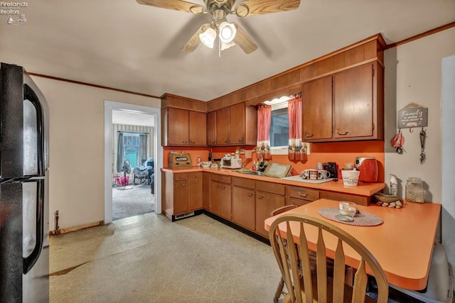 kitchen featuring a sink, light countertops, ceiling fan, freestanding refrigerator, and brown cabinets