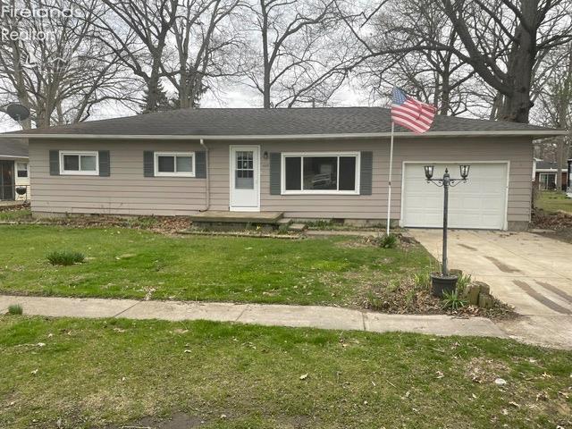 single story home with concrete driveway, a front yard, and an attached garage
