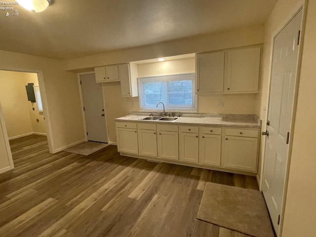 kitchen with baseboards, light countertops, white cabinetry, a sink, and wood finished floors