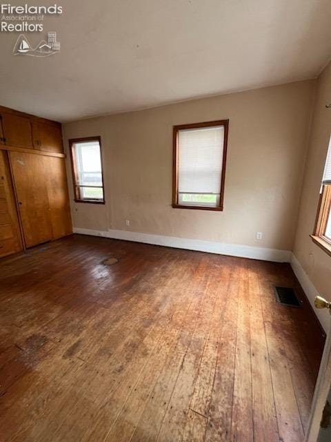 unfurnished bedroom with wood-type flooring, baseboards, a closet, and visible vents