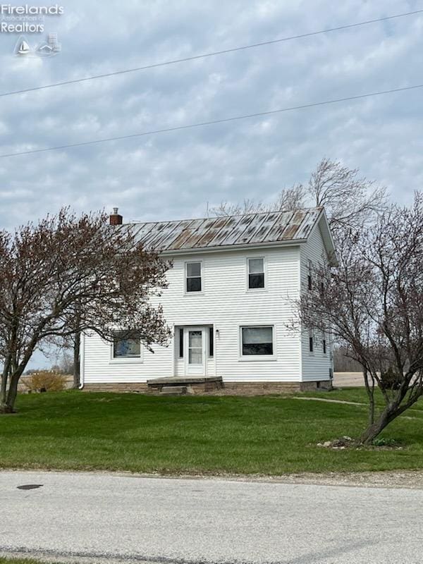 view of front of property featuring a chimney, a standing seam roof, a front yard, and metal roof