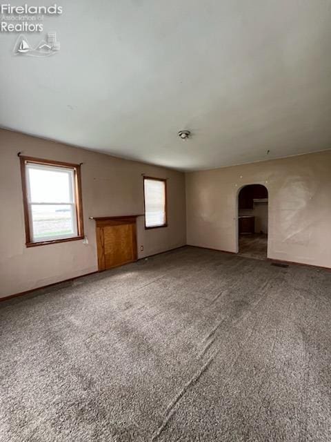 unfurnished living room with arched walkways and carpet