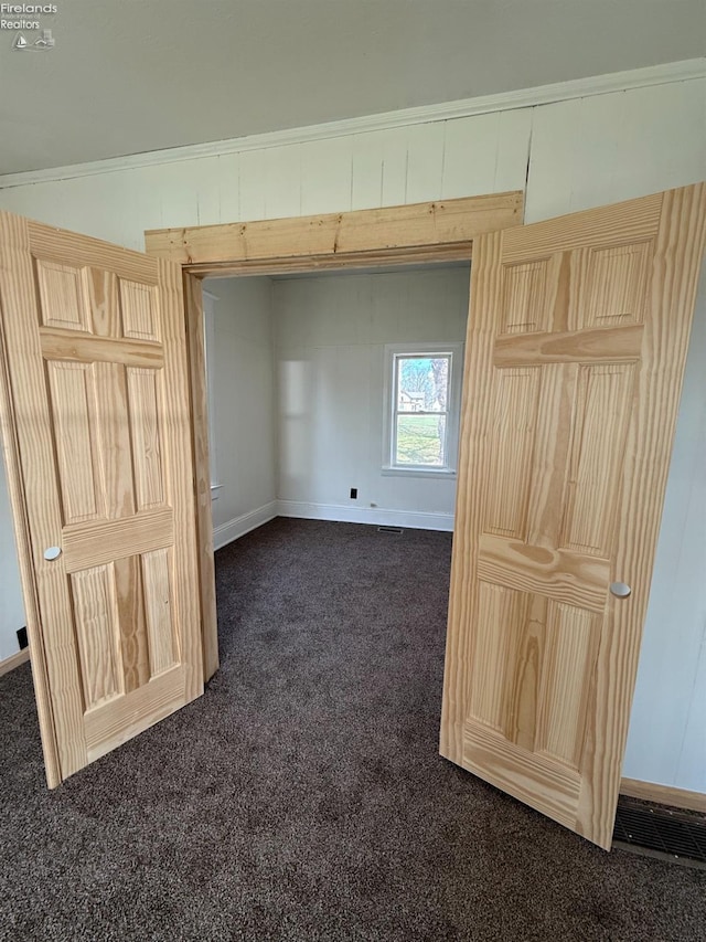 unfurnished bedroom with baseboards, dark colored carpet, and visible vents