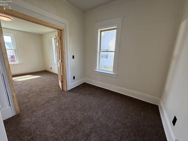 spare room with a healthy amount of sunlight, dark colored carpet, and baseboards