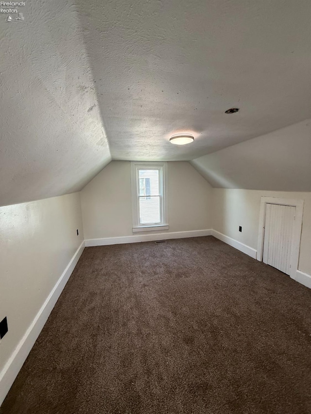 bonus room featuring baseboards, lofted ceiling, and dark colored carpet