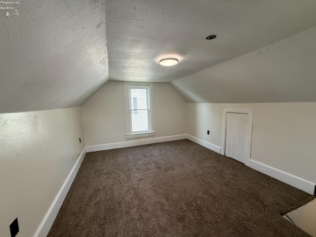 additional living space with dark colored carpet, baseboards, a textured ceiling, and lofted ceiling