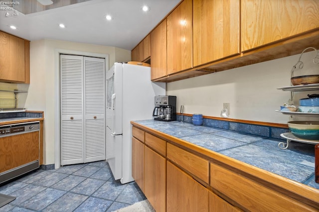 kitchen with recessed lighting, stone finish floor, dishwasher, freestanding refrigerator, and brown cabinetry