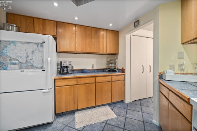 kitchen with brown cabinetry, recessed lighting, tile countertops, and freestanding refrigerator