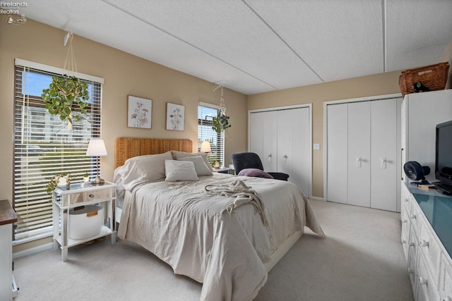 bedroom featuring two closets, light carpet, and a textured ceiling
