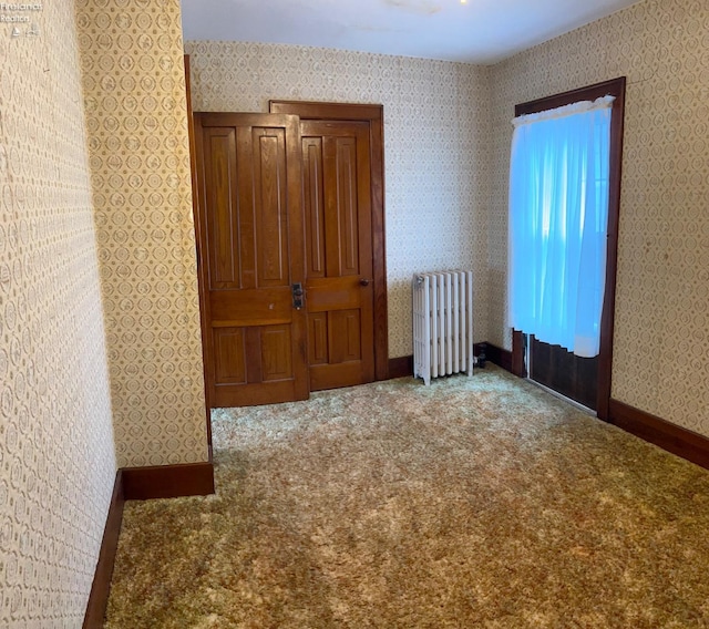 carpeted empty room featuring baseboards, radiator, and wallpapered walls