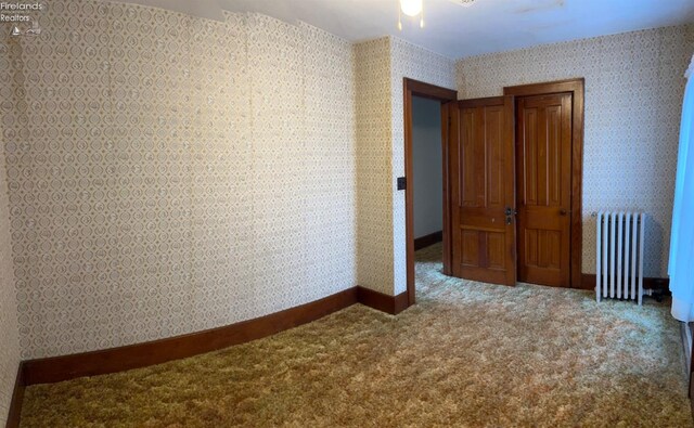 carpeted empty room with baseboards, radiator, and ceiling fan