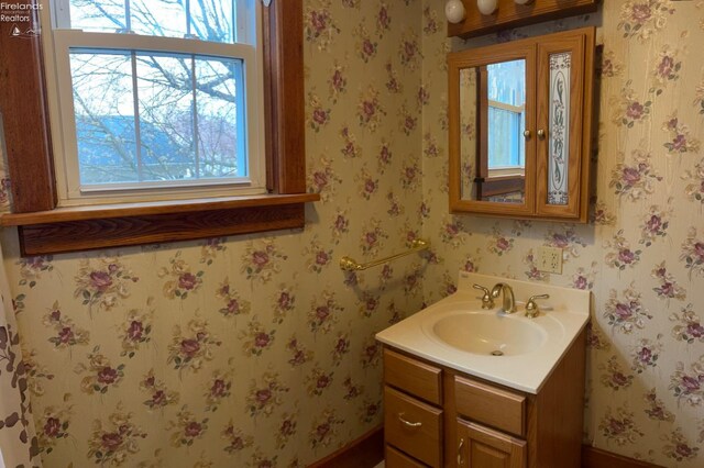 bathroom featuring vanity, baseboards, and wallpapered walls