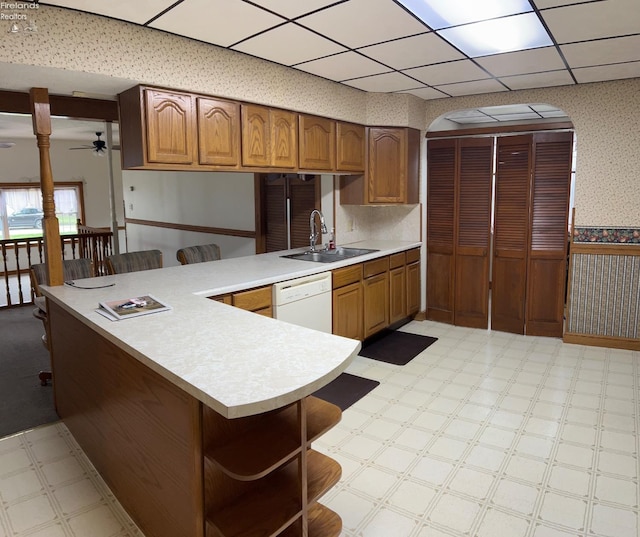 kitchen featuring wallpapered walls, light floors, arched walkways, dishwasher, and a sink