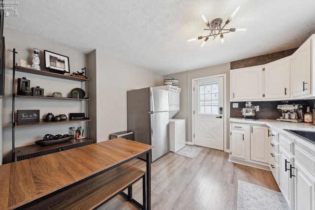 kitchen featuring white cabinets, light countertops, freestanding refrigerator, a textured ceiling, and light wood-style flooring