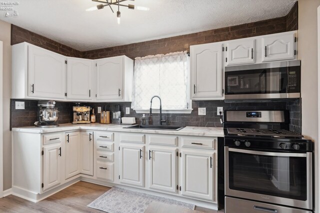 kitchen with light countertops, white cabinets, appliances with stainless steel finishes, light wood finished floors, and a sink