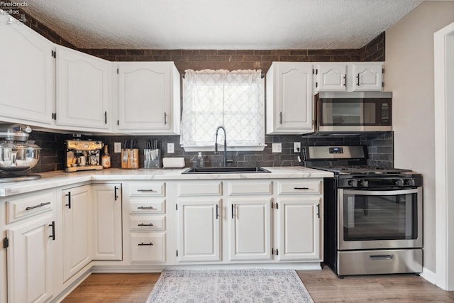 kitchen with a sink, light countertops, a textured ceiling, white cabinetry, and stainless steel appliances