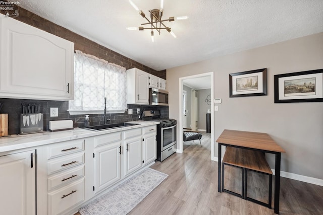 kitchen featuring white cabinets, a chandelier, a sink, stainless steel appliances, and decorative backsplash