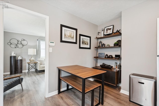 dining room with light wood-style flooring, baseboards, and a textured ceiling