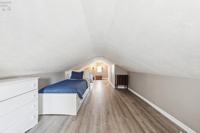 unfurnished bedroom featuring vaulted ceiling, baseboards, a textured ceiling, and wood finished floors