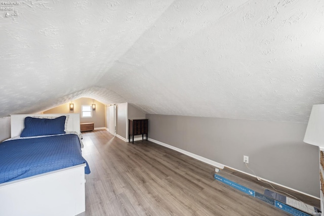 unfurnished bedroom with a textured ceiling, wood finished floors, baseboards, and vaulted ceiling