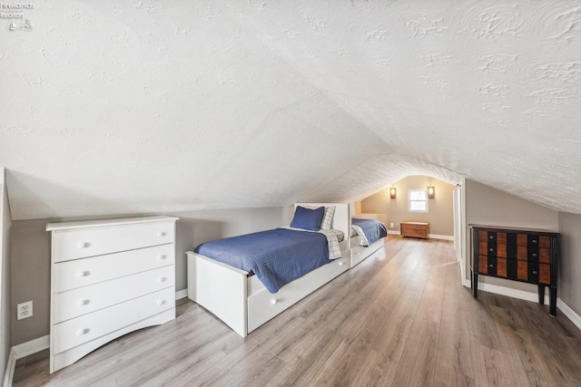 bedroom featuring vaulted ceiling, wood finished floors, and a textured ceiling