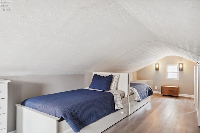 bedroom featuring baseboards, lofted ceiling, wood finished floors, and a textured ceiling