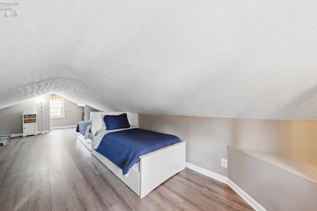 bedroom with a textured ceiling, wood finished floors, baseboards, and vaulted ceiling