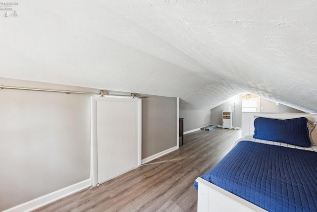 unfurnished bedroom with a textured ceiling, wood finished floors, baseboards, and vaulted ceiling