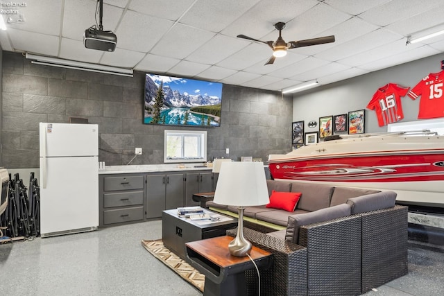 interior space featuring a paneled ceiling, a ceiling fan, and concrete block wall