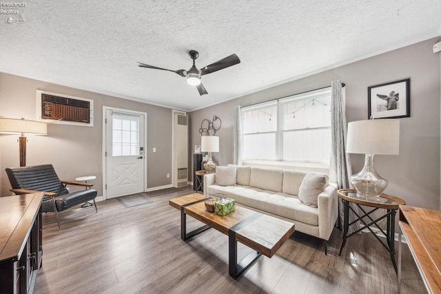 living room featuring ornamental molding, a textured ceiling, a ceiling fan, light wood-style floors, and a wall unit AC