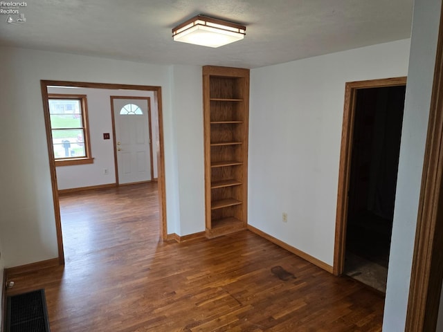 unfurnished room featuring built in shelves, visible vents, baseboards, and dark wood-style floors