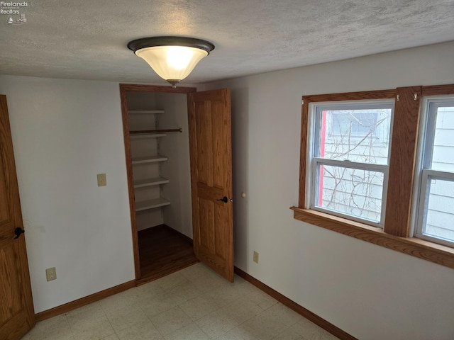 unfurnished bedroom with a closet, baseboards, light floors, and a textured ceiling