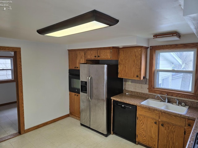kitchen with brown cabinets, a sink, black appliances, and dark countertops
