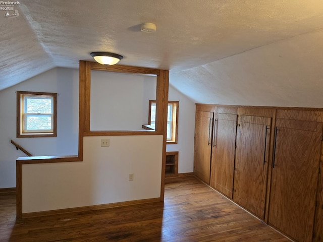 additional living space with baseboards, a textured ceiling, wood finished floors, and lofted ceiling