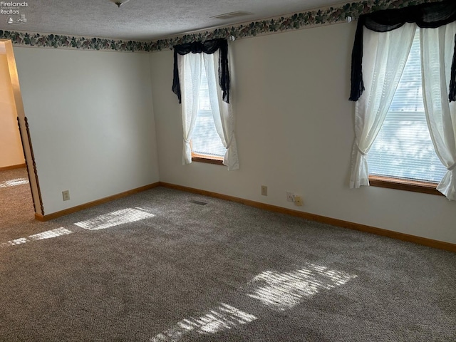 carpeted spare room featuring a textured ceiling, visible vents, and baseboards