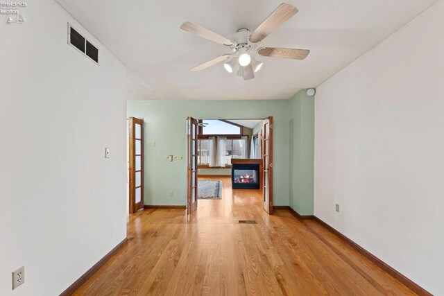 1001 Birchwood Dr, Sandusky, OH 44870 - spare room with light wood finished floors, a glass covered fireplace, baseboards, visible vents, and ceiling fan