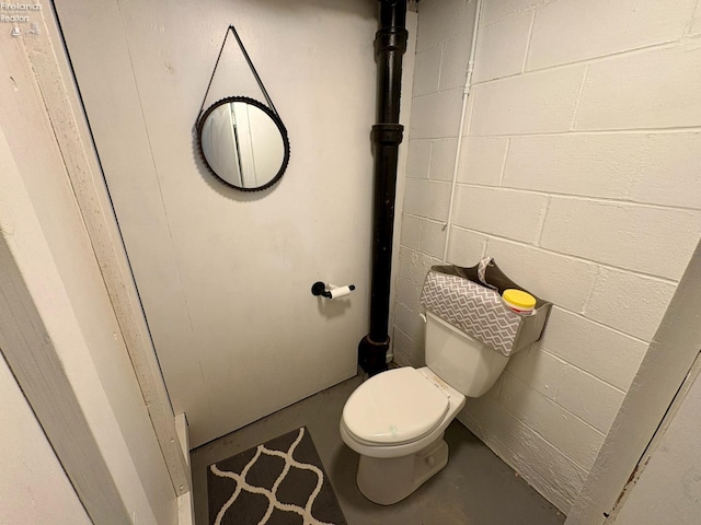 bathroom featuring concrete block wall, toilet, and finished concrete floors